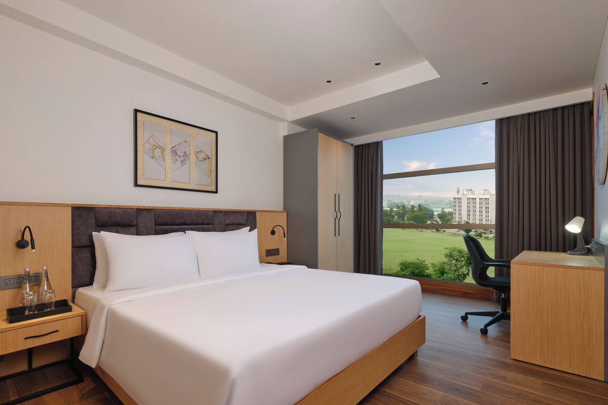 Habitación de hotel moderna con una cama grande, un escritorio, una silla y vistas de la ciudad.