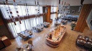 A modern dining area with multiple tables and chairs, a central decorative island, and hanging light fixtures. - Regenta - The World Surat (Surat)