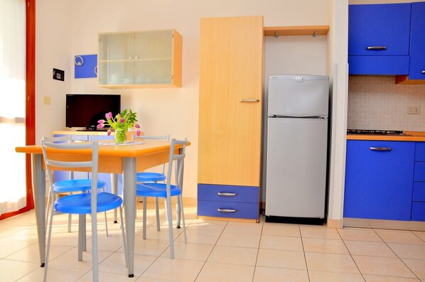 Eine kompakte Küche mit Kühlschrank, einem Esstisch mit Stühlen und blauen Schränken.