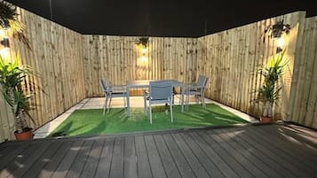 A wooden deck with a table and chairs, surrounded by a wooden fence and potted plants.