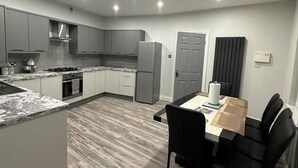 A modern kitchen with grey cabinets, a built-in oven, and a dining area with a table and chairs. - Immaculate 4-bed Detached House in Bootle (Bootle)