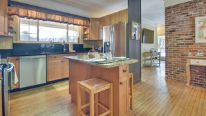 Eine Küche mit Holzschränken, einem Edelstahlkühlschrank, einer Arbeitsplatte aus Granit und einem hölzernen Hocker.