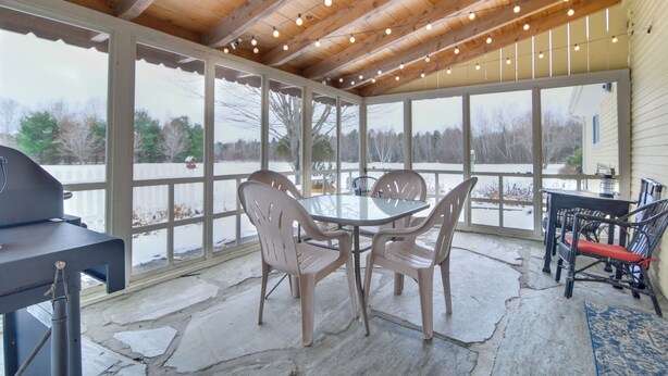 Eine überdachte Terrasse mit Tisch und Stühlen, einem Grill und Blick auf eine verschneite Landschaft.