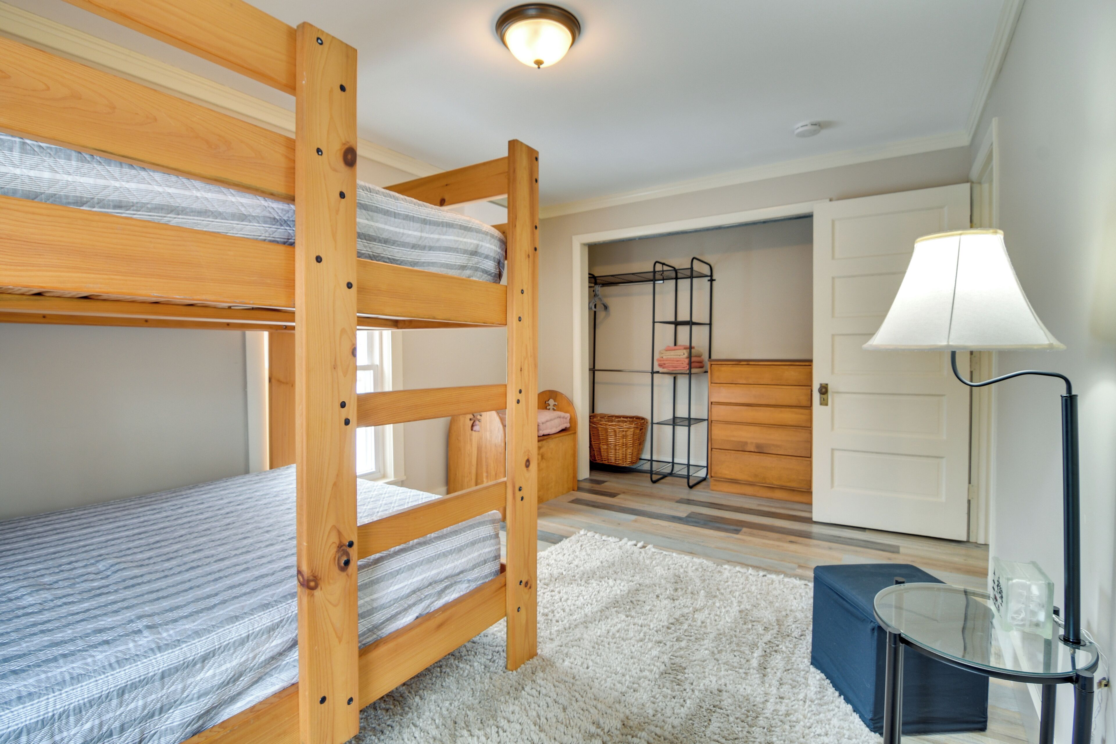 A room with bunk beds, a small table, a lamp, and a wardrobe.