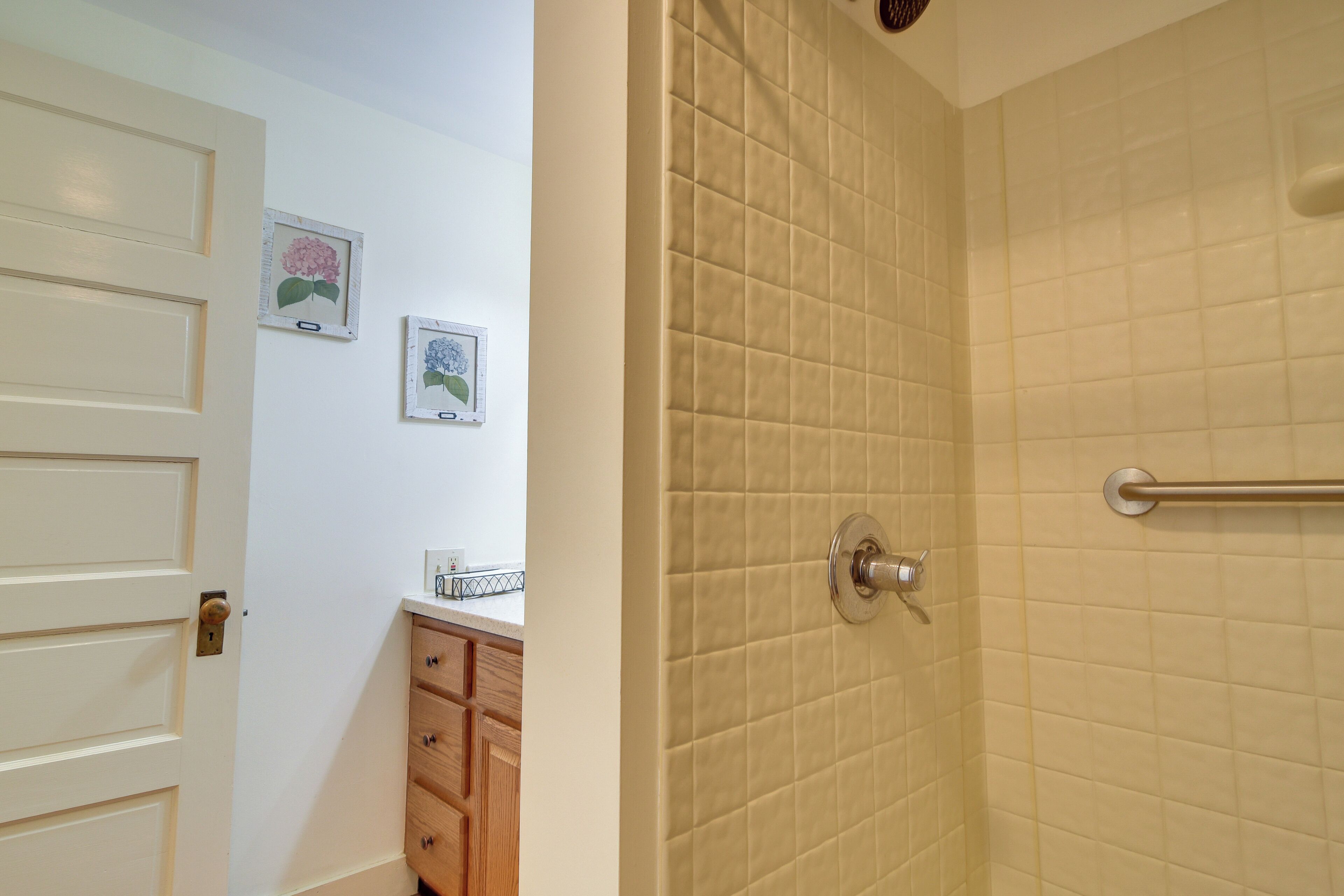 Une salle de bain avec un mur de douche recouvert de carreaux beiges, une porte avec une serrure et un meuble en bois doté de tiroirs.