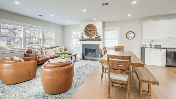 A spacious living room with a fireplace, a dining area with wooden furniture, and a kitchen with white cabinets.