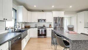 A modern kitchen with white cabinets, granite countertops, stainless steel appliances, and a central island with bar stools.