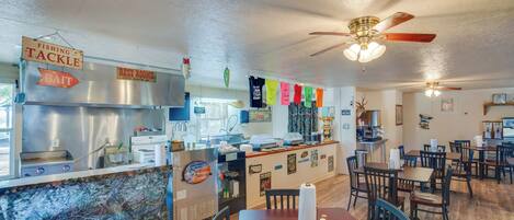 A restaurant interior with a counter, dining tables, chairs, ceiling fans, and various signs.
