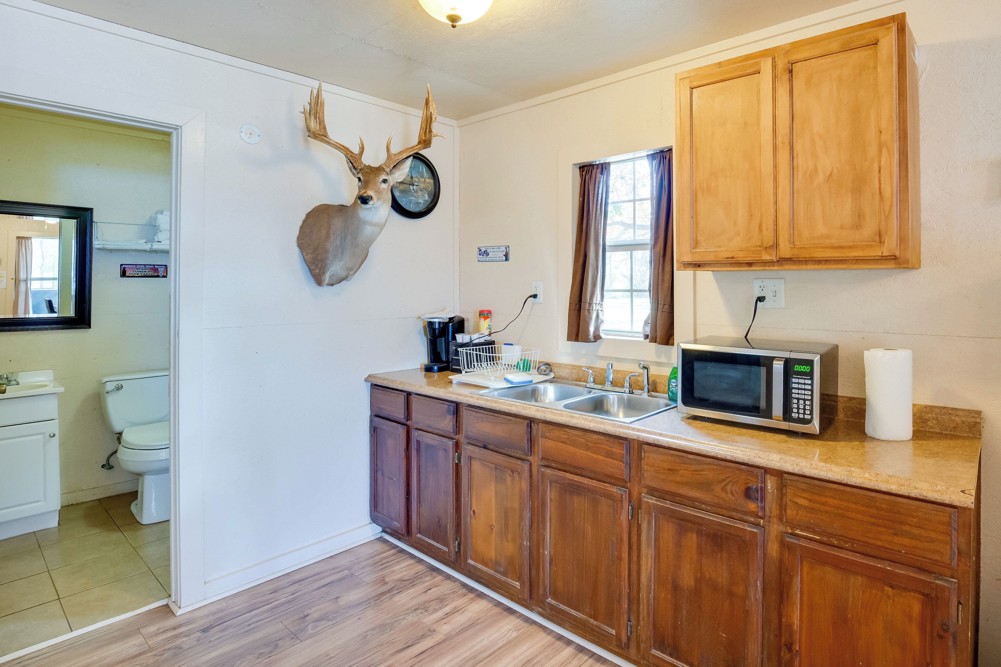 A kitchen with wooden cabinets, a microwave, a sink, and a deer head mounted on the wall.