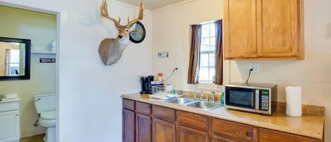 A kitchen with wooden cabinets, a microwave, a sink, and a deer head mounted on the wall.