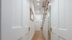 A hallway with white doors, wooden flooring, and a staircase leading to an upper level. - West London Period Home (London)