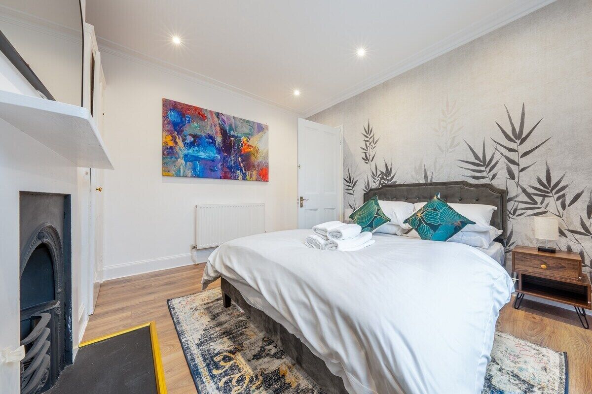 A modern bedroom with a large bed, a fireplace, a colorful abstract painting, and a decorative wall with leaf patterns.