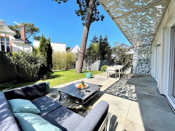 A patio with a sofa, a table with fruit, a pergola, and a view of the backyard.