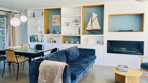 En moderne stue med en blå sofa, et spisebord med stole og indbyggede reoler med dekorative genstande.