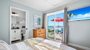 Een slaapkamer met een bed, een dressoir, een kaptafel en een groot raam met uitzicht op het strand.