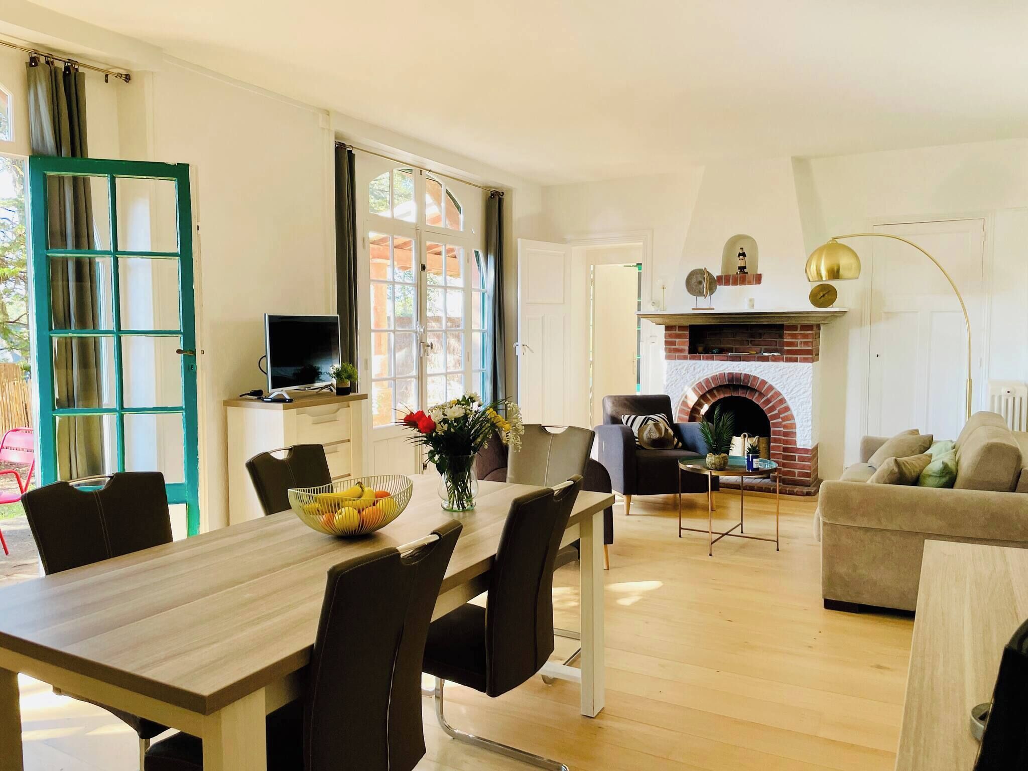 Un comedor con una mesa y sillas de madera, un televisor sobre un mueble bajo y una chimenea de ladrillo.