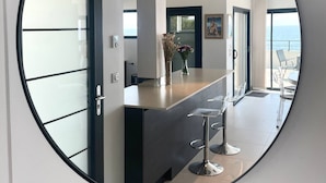 A modern kitchen with a dark countertop, a round mirror, and a view of the sea through large windows. - L'écrin marin : Vue exceptionnelle sur l'Océan (Batz-sur-Mer)