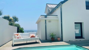 A modern outdoor pool area with a white lounge chair and potted plants. - L'écrin marin : Vue exceptionnelle sur l'Océan (Batz-sur-Mer)