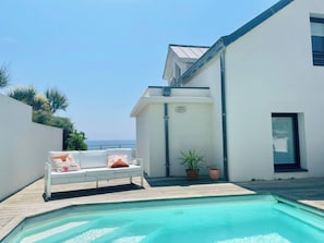 Uma área de piscina moderna ao ar livre, com uma espreguiçadeira branca e plantas em vasos.