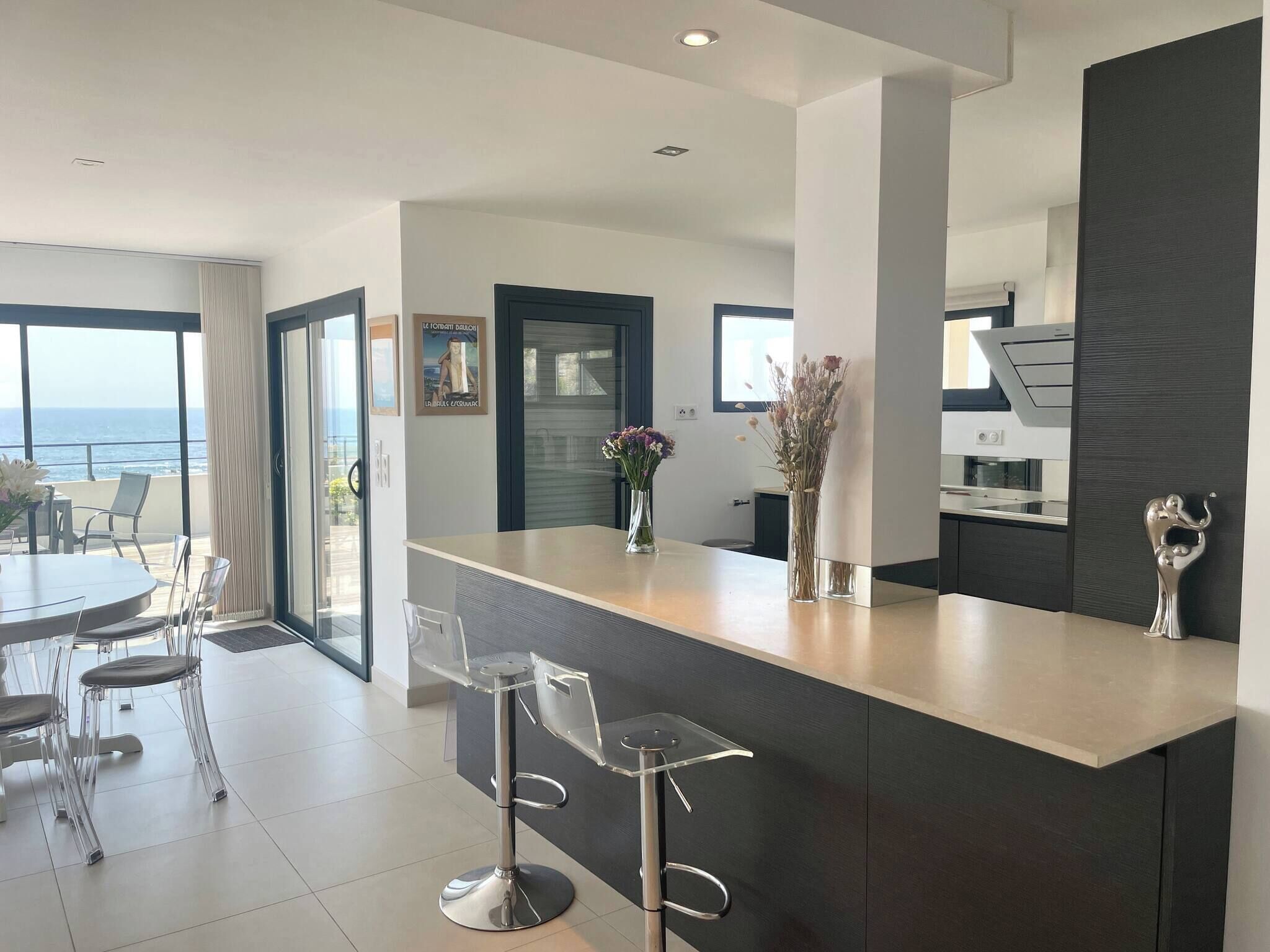 Una cocina moderna con barra, una mesa de comedor con sillas y vista al océano.