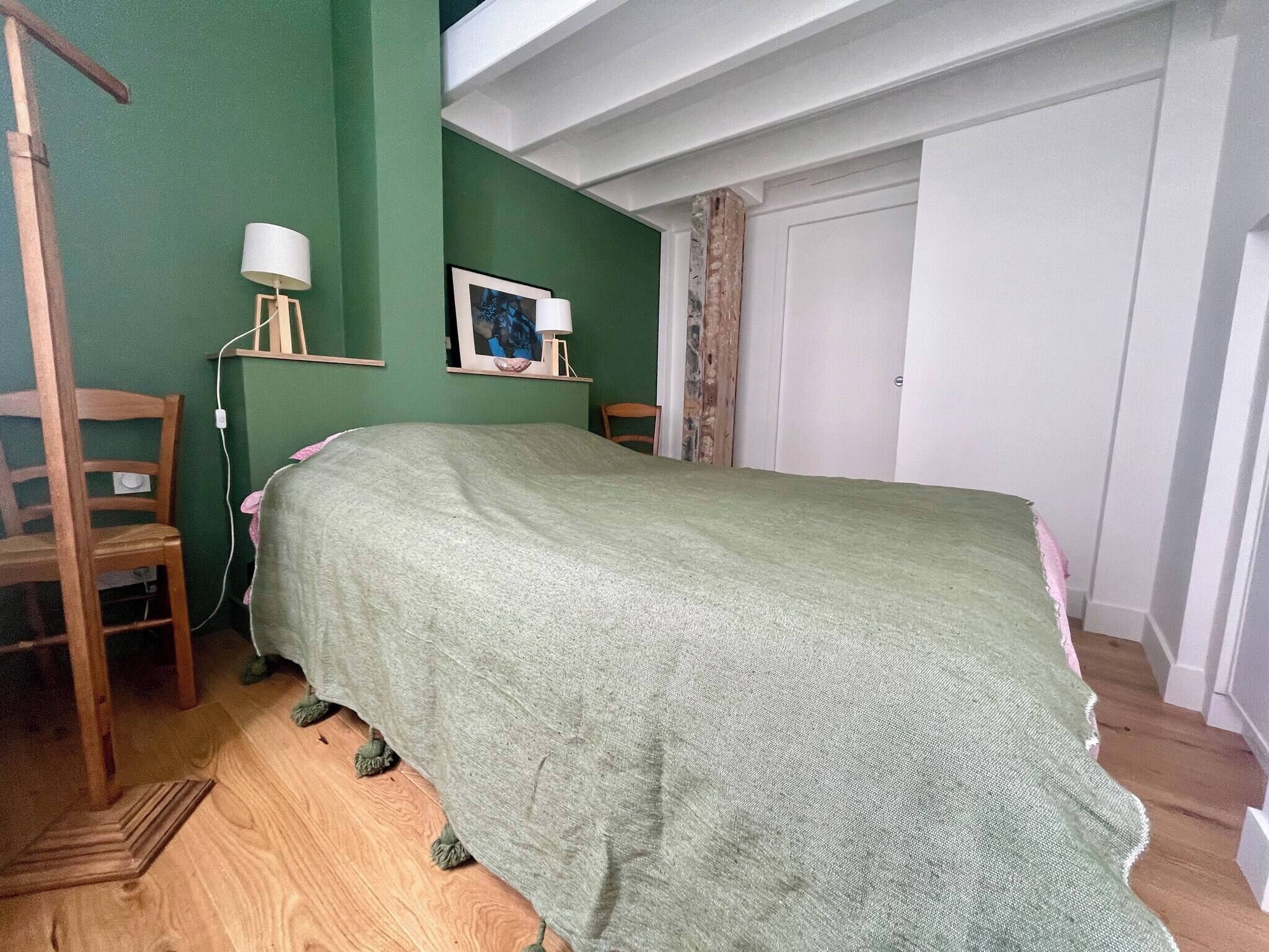 A bedroom with a bed, a wooden chair, a lamp, and a framed picture on the wall.