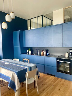 A modern kitchen with blue cabinets, a dining table with a blue tablecloth, and a white chair. - FACE SEA La Baule Le Panoramique (La Baule-Escoublac)