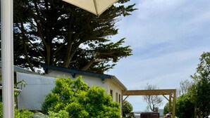 Un espacio de comedor al aire libre con una mesa para dos, una cesta de frutas y una pérgola al fondo.