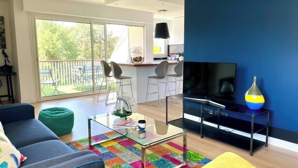 Un salon moderne avec une grande télévision, un tapis coloré et un balcon doté d’un espace salon extérieur.
