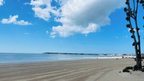 Une plage avec un ciel dégagé, un rivage sablonneux et une côte lointaine parsemée de bâtiments.