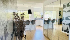 Une cuisine moderne avec des meubles blancs, un luminaire suspendu noir et un coin repas avec des chaises noires.