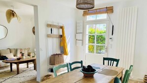 Un comedor con una mesa de madera, sillas verdes, una lámpara de techo tejida y una ventana con persianas.