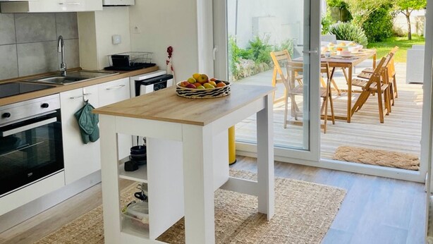 Una cocina moderna con armarios blancos, una mesa de madera y una cesta de fruta.