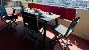 Een balkon met een tafel gedekt voor twee personen, stoelen en uitzicht op een jachthaven met boten en gebouwen.