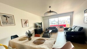 Een woonkamer met een eettafel, stoelen, een bank, een televisie en kunstwerken aan de wanden.