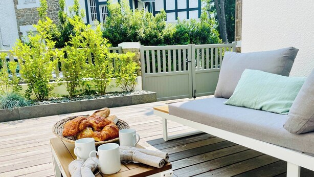 Una terraza de madera con un sofá blanco y una mesa con pan, tazas y toallas.