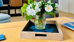 Una cocina moderna con salpicadero de mármol, una zona de comedor con sillas de mimbre y un jarrón con flores blancas sobre una mesa de madera.