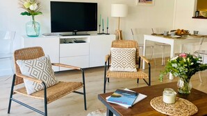 A living room with a TV, two wicker chairs, a coffee table, and a dining area with a white table and chairs. - Appartement La baule "Le 30" (La Baule-Escoublac)