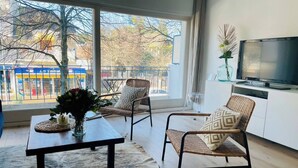 A modern living room with a large window, a flat-screen TV, two wicker chairs, a wooden table, and a fur rug. - Appartement La baule "Le 30" (La Baule-Escoublac)