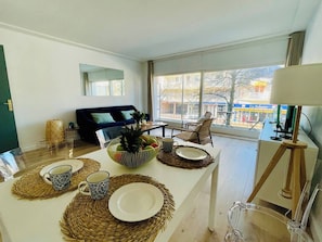 Un salon moderne avec une table à manger pour deux personnes, un canapé et une grande fenêtre donnant sur l’extérieur.