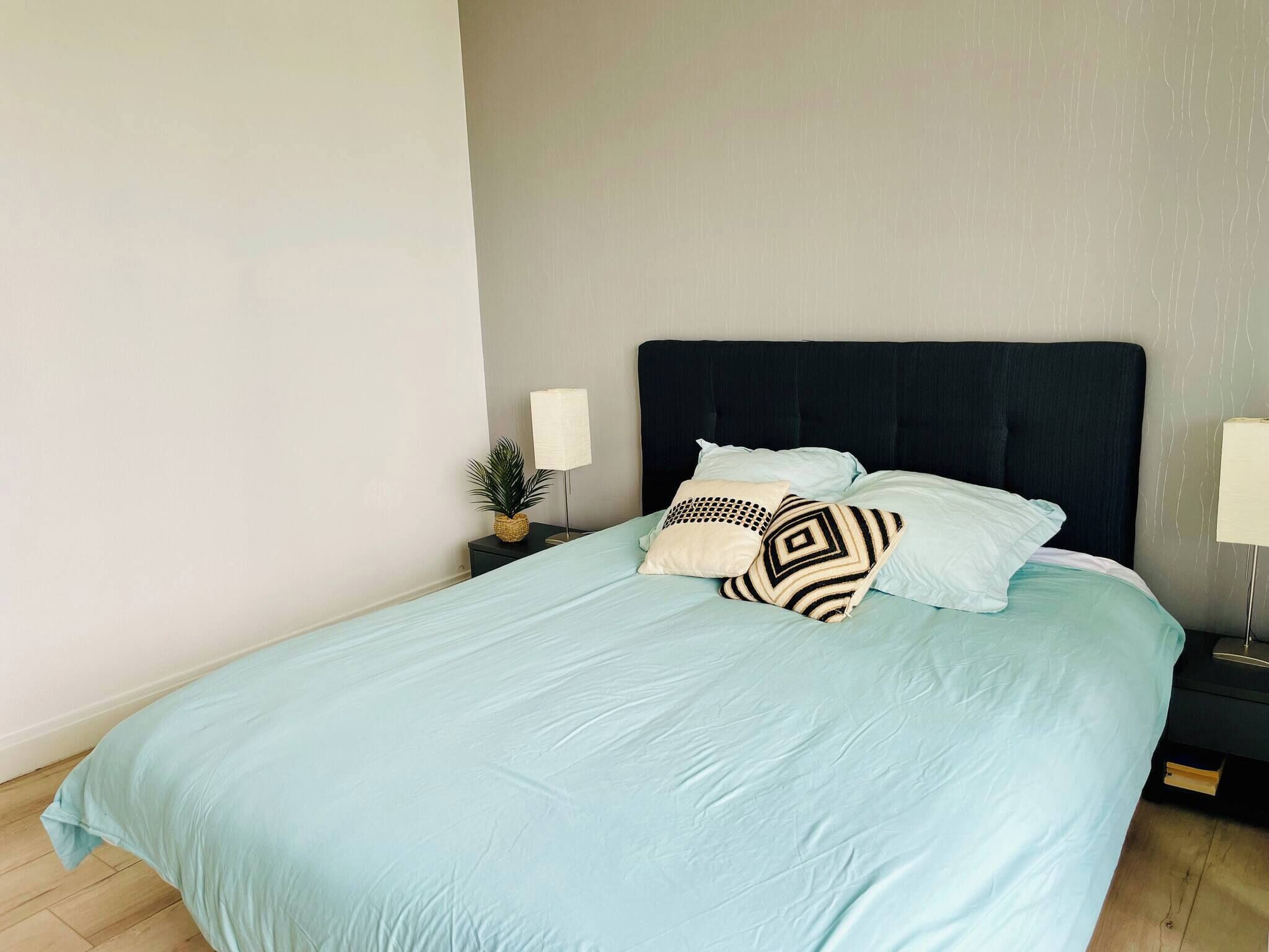Una cama con una colcha azul claro, un cabecero oscuro y dos lámparas de noche.