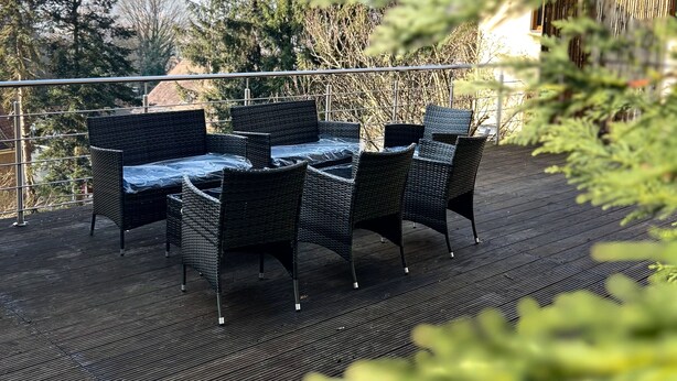 Eine Terrasse im Freien mit Korbmöbeln und Blick auf hohe Bäume.