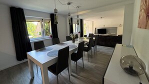 Ein moderner Essbereich mit einem weißen Tisch, schwarzen Stühlen und einem Fernseher im Hintergrund.