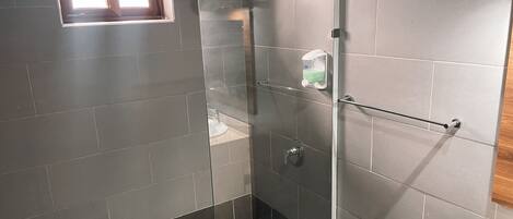 Een moderne badkamer met een douchecabine van glas, een klein raam en een betegelde vloer.