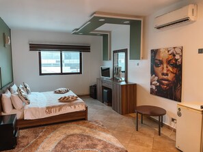 Un dormitorio con cama, escritorio, silla, televisor, un cuadro y aire acondicionado.