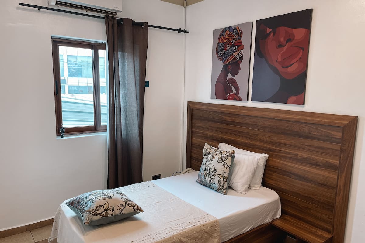 Un dormitorio con cabecera de madera, una cama con ropa de cama blanca, una ventana con cortinas y dos obras de arte colgadas en la pared.