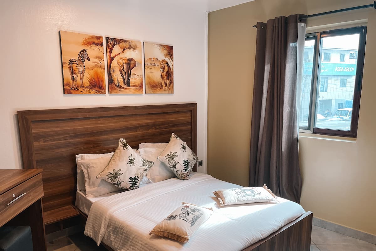 Una cama bien hecha con almohadones florales, un cabecero de madera y tres cuadros con motivos de animales salvajes encima.