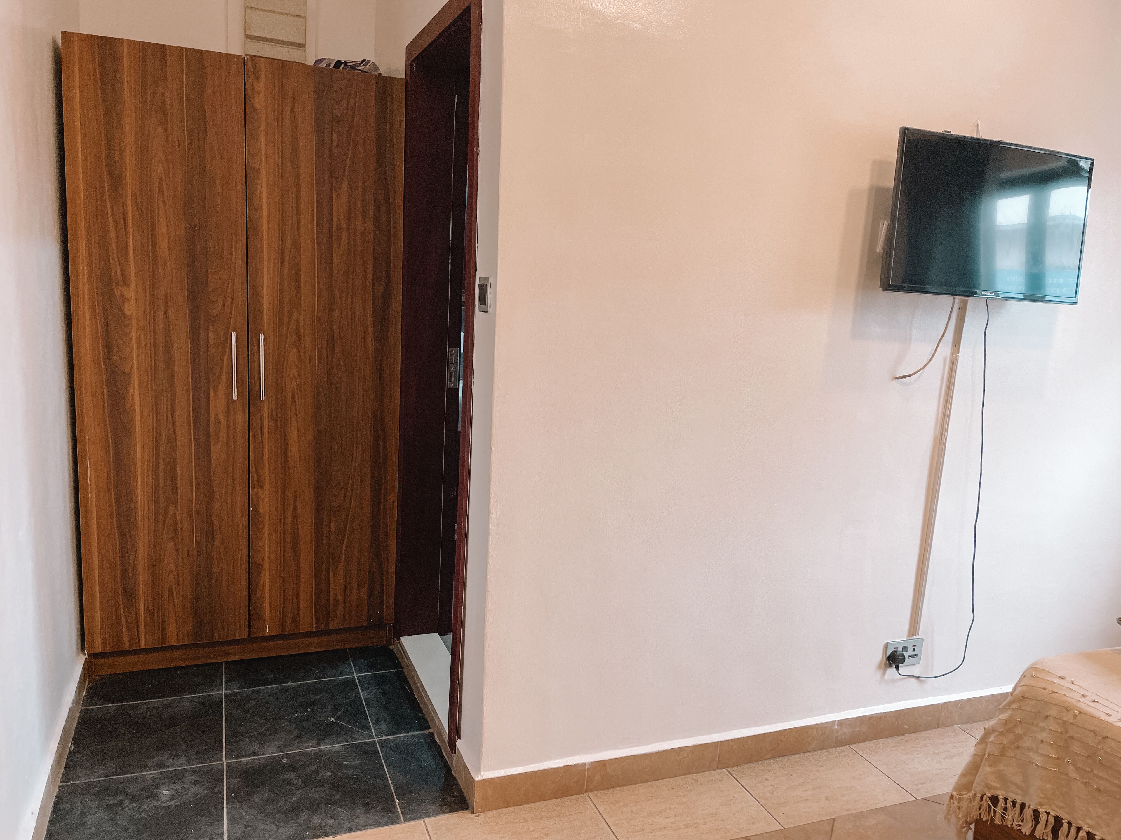 Una stanza con un armadio in legno, una televisione fissata al muro e un pavimento piastrellato.