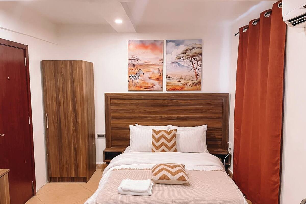 Una cama bien hecha con cabecera de madera, un par de almohadas estampadas con patrón chevron y una toalla blanca doblada.