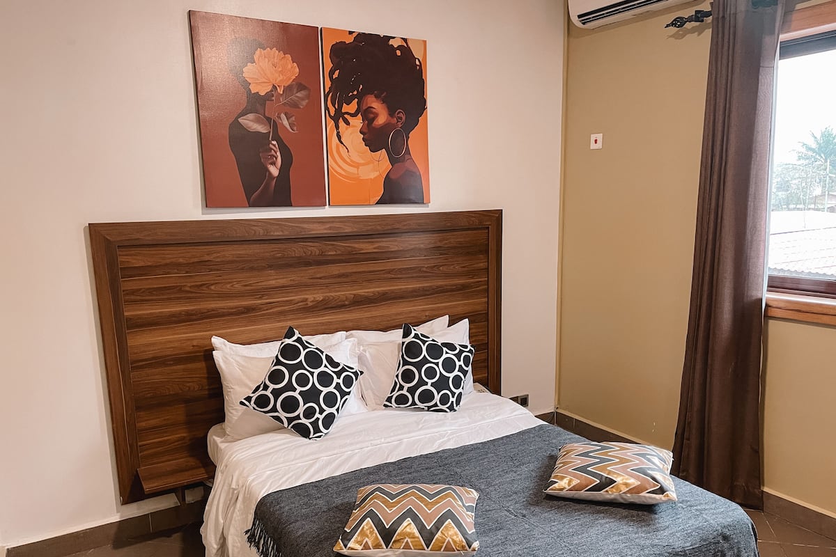 Una cama con cabecera de madera, ropa de cama blanca y almohadas estampadas.