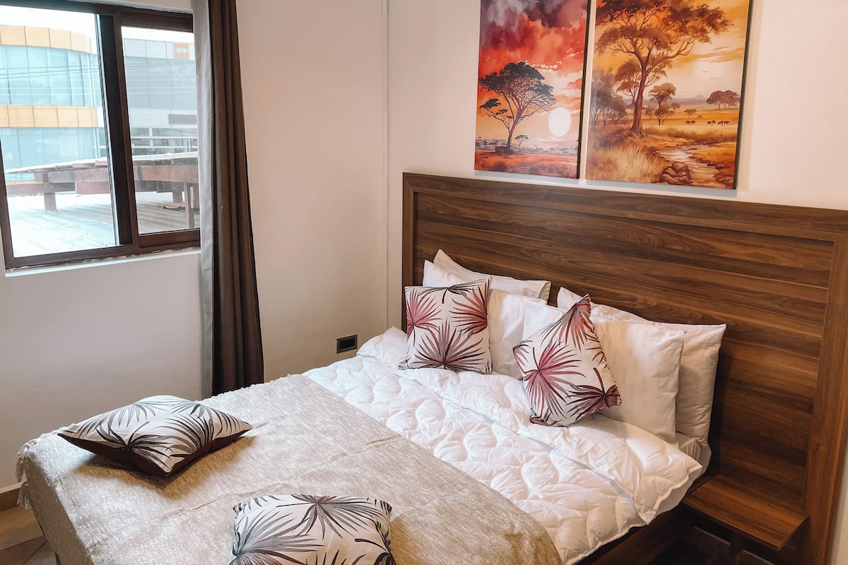 Una habitación de hotel con una cama, ropa de cama blanca y dos cuadros de paisajes.